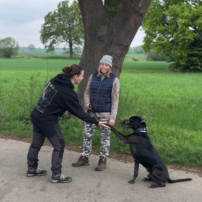 Hundetrainerin Kristina mit schwarzem Hund mit Maulkorb beim Pfötchen geben – Hundeschule Göttingen